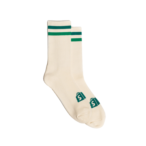 A pair of cream & green colored Shopify Supply Business as Usual Socks with the green Shopify logo on the top of the foot.